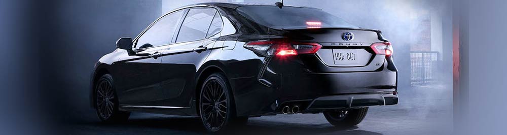 A picture of a 2023 Toyota Camry LE with the midnight black exterior paint color option, taken from the back driver's side corner angle in a fogging parking garage.