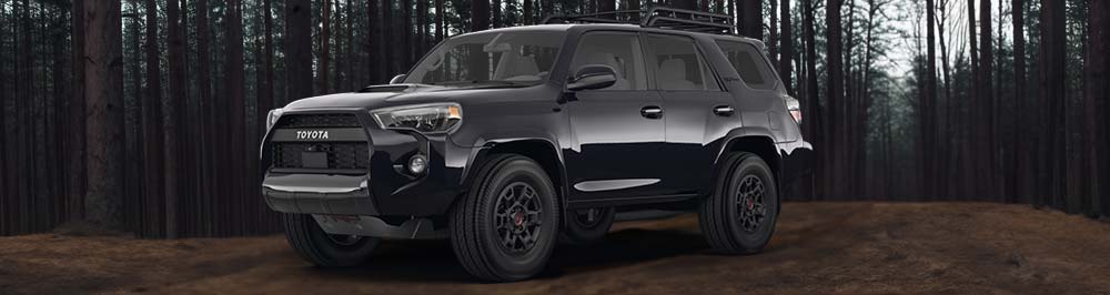 A picture of a 2023 black trd pro 4runner with the midnight black metallic exterior paint color option, with the SUV parked off road in a forest