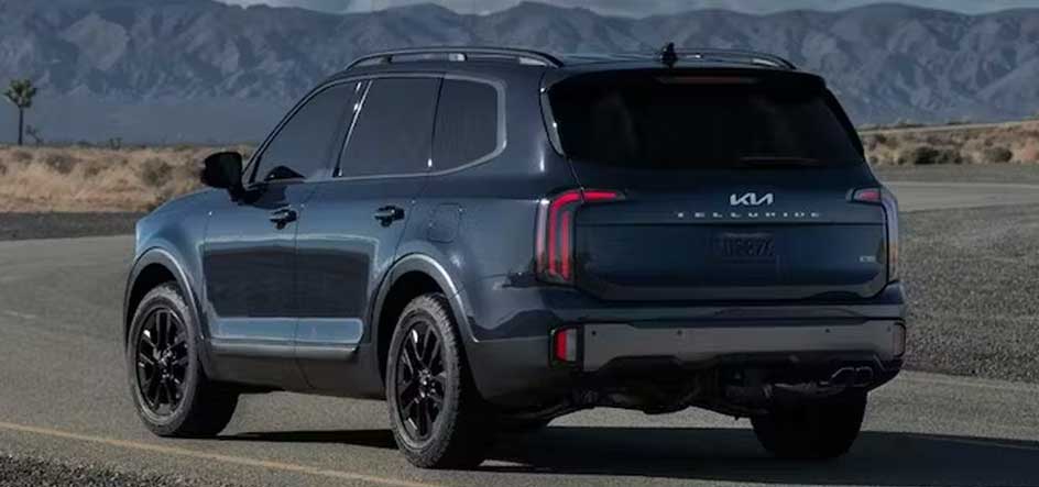 A picture of a blue 2023 Kia Telluride driving away on a road with mountains in the background